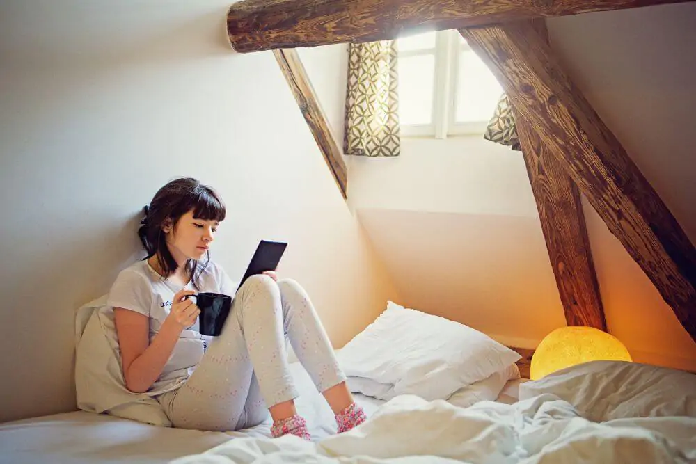 A young teenager girl is focused reading an electronic romance with her ebook reader while she is on the bed